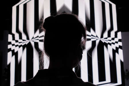 NIZHNY NOVGOROD, RUSSIA - AUGUST 27, 2021: Digital Festival. Woman looking at large projection cube wall screen with rotating hypnotic optical illusion in low light room. Video mapping show conceptのeditorial素材