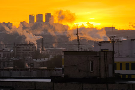Roofs of old apartment buildings with TV antennas and white smoke from smokestack against morning orange sunrise sky. Cityscape, urban, industrial and architecture conceptの写真素材