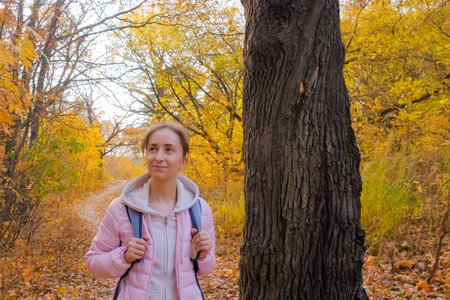 Young woman with backpack walking in autumn park, forest. Active outdoor lifestyle, leisure time,...