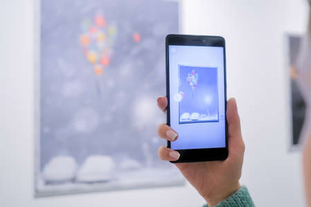 MOSCOW, RUSSIA - JANUARY 5, 2020: AR Exhibition. Woman using smartphone with augmented reality app - interactive picture, illustration with movement. Future, digital, contemporary art conceptのeditorial素材