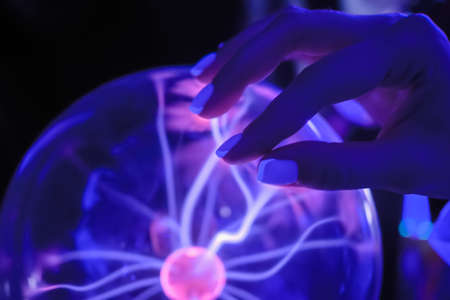 Woman hand touching plasma ball with many energy rays inside - close up view. Electricity, education, science, futuristic and physics conceptの写真素材