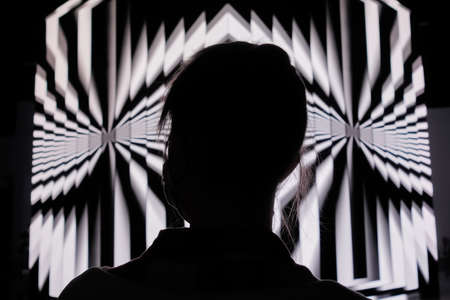NIZHNY NOVGOROD, RUSSIA - AUGUST 27, 2021: Digital Festival. Woman looking at large projection cube wall screen with rotating hypnotic optical illusion in low light room. Video mapping show conceptのeditorial素材