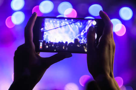 Woman hands silhouette taking photo or recording video of live music concert with smartphone in front of stage of nightclub - close up. Photography, entertainment, technology conceptの写真素材