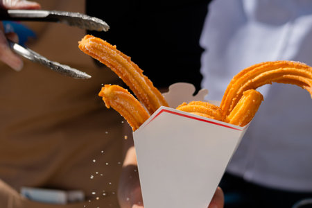 Homemade crunchy churros in white paper box at summer outdoor food market - close up. Traditional Spanich cuisine, bakery, cookery, gastronomy and street food conceptの写真素材