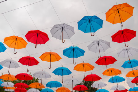Colorful umbrellas hanging against gray overcast sky and swaying in wind at summer city festival - low angle view. Street decoration, celebration, art, holiday conceptの写真素材
