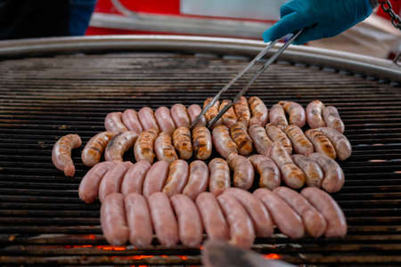 Close up: chef grilling fresh meat sausages on big round hanging grill at summer local food market. Outdoor cooking, barbecue, gastronomy, cookery, street food conceptの写真素材