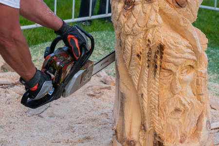NIZHNY NOVGOROD, RUSSIA - JUNE 15, 2020: Summer Outdoor Festival. Man carpenter, wood sculptor using chainsaw for carving wooden sculpture. Carpentry, craftsmanship, design conceptのeditorial素材