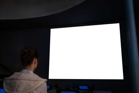 Woman looking at large wall blank interactive white display in dark room of modern technology exhibition, museum or cinema. Mock up, white screen, futuristic, template, education conceptの写真素材