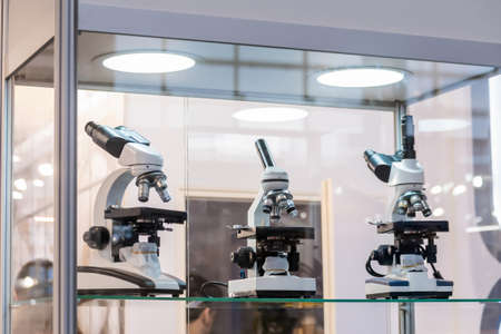 Three microscopes in glass showcase at science exhibition, trade show. Laboratory equipment, medical, optical, pharmaceutical and education conceptの写真素材
