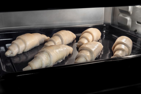 Six uncooked croissants on tray in electric oven. French cuisine, homemade bakery, breakfast, food,...