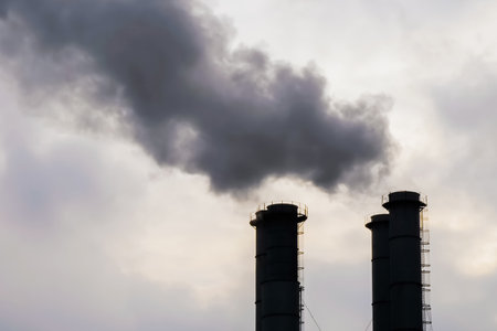 Factory smokestack, chimney silhouettes emitting smoke against grey sky. Environmental pollution, ecology problems, industrial emissions, manufacturing conceptの写真素材