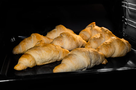 Eight baked croissants on tray in electric oven. French cuisine, homemade bakery, breakfast, food,...