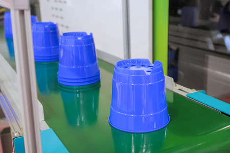 Moving polypropylene purple pots on conveyor belt of plastic injection molding machine with robotic arm at exhibition, trade show. Manufacturing, industry and automated technology equipment conceptの写真素材