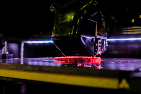 Automatic three dimensional printer machine printing red flat plastic model at modern technology exhibition - close up. 3D printing, futuristic, prototype, manufacturing and production conceptの写真素材