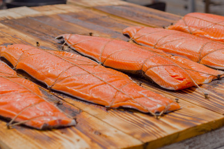 Close up: hot smoked red salmon fish in row on wooden board at summer outdoor food festival, market. Preparation, cookery, gastronomy and street food conceptの写真素材