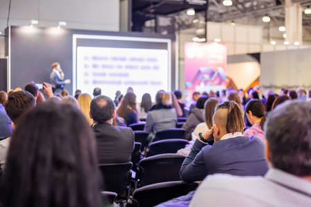 Back view of unrecognizable people, audience listening lecture, presentation at trade show, conference hall. Business, congress, seminar, corporate, training, education conceptの写真素材