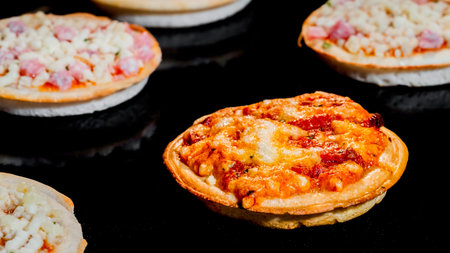 One of many mini pizzas with ham, cheese baking on tray in electric oven - close up view. Italian cuisine, individuality, cooking conceptの写真素材