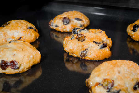 Many baked homemade orange crunchy oatmeal raisin cookies on metal sheet in oven - close up. Dessert, gastronomy, baking and food conceptの写真素材