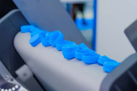 Production line - many blue plastic bottle caps falling from conveyor belt of automatic molding machine at factory, exhibition: close up. Manufacturing, recycling, industry, technology conceptの写真素材