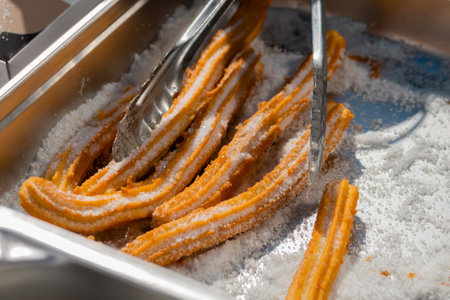 Chef preparing homemade crunchy churros with powdered sugar at summer outdoor food market - close up...