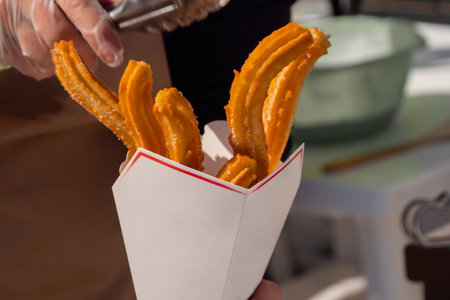 Chef woman holding paper box with homemade crunchy churros at summer outdoor food market - close up. Traditional Spanich cuisine, bakery, cookery, gastronomy and street food conceptの写真素材