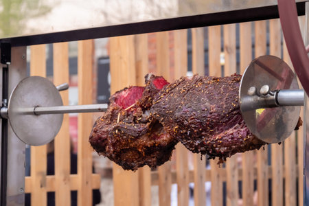 Process of cooking large meat peaces on spit over open fire at summer historical food festival, market - close up view. Outdoor cooking, travelling, camping, reenactment conceptの写真素材