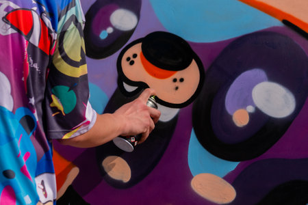 MOSCOW, RUSSIA - APRIL 5, 2019: Summer Graffiti Festival. Man hand holding aerosol spray and painting colorful graffiti on wooden surface. Urban culture, outdoor activity, freedom, creativity conceptのeditorial素材