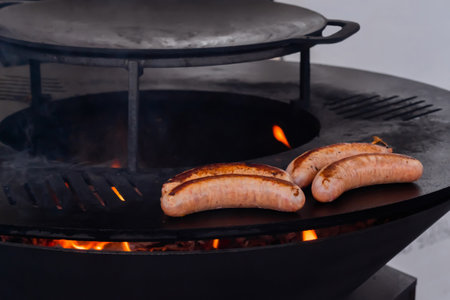 Process of grilling fresh meat sausages on black brazier at summer local food market: close up view. Outdoor cooking, barbecue, gastronomy, cookery, street food conceptの写真素材