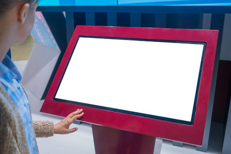 Mockup: woman looking at blank white interactive touchscreen display of electronic kiosk at...