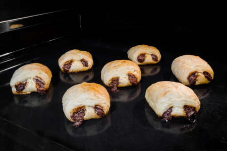 Seven mini puff pastry buns with chocolate filling baking and rising on tray in electric oven....