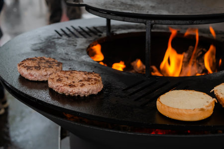 Process of grilling fresh meat cutlets and buns for burgers on brazier with hot flame at summer local food market - close up view. Outdoor cooking, gastronomy, cookery, street food conceptの写真素材