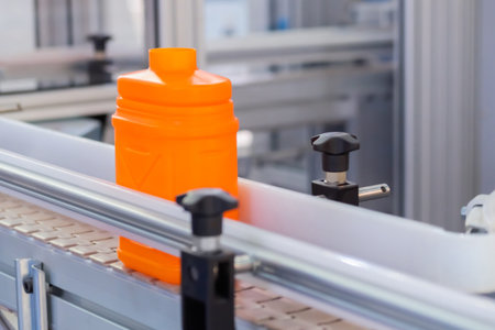 Empty orange plastic jerrycan moving on conveyor belt of automatic pet blow molding machine at...