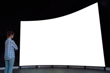Woman looking at large wall blank interactive white display in dark room of modern technology exhibition or museum. Mock up, white screen, futuristic, template, education conceptの写真素材