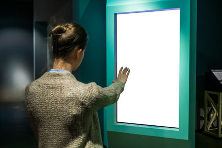 Woman using white blank interactive touchless vertical display of electronic multimedia kiosk with no touch control in dark room. Mock up, copyspace, template and technology conceptの写真素材
