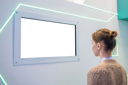 Woman looking at blank digital interactive white display wall at exhibition or museum with futuristic scifi interior. White screen, mock up, future, copyspace, template, technology conceptの写真素材