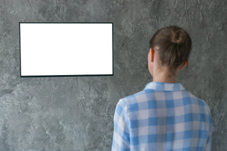 Mockup image - woman watching flat smart led TV with white blank screen hanging on wall in the living room at home. Mock up, copyspace, leisure time, template, entertainment and technology conceptの写真素材