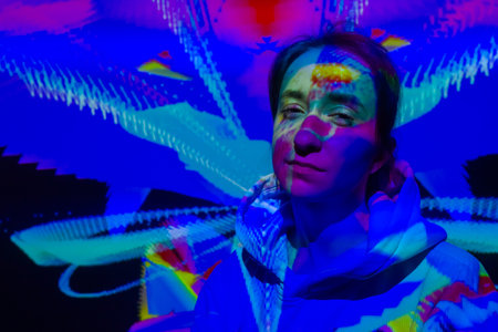 NIZHNY NOVGOROD, RUSSIA - JANUARY 8, 2022: AR event - front view: portrait of woman looking at camera at immersive exhibition with colorful projector light: digital art installationのeditorial素材