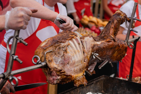 Process of cooking roasted pork on spit at summer outdoor food market, chef cutting meat - close up view. Professional cooking, cookery, gastronomy and street food conceptの写真素材
