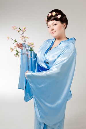 woman in blue kimono with a branch of cherry blossoms .の写真素材