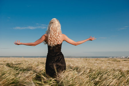 Girl in a black dress standing in a wheat field arms spreadの写真素材