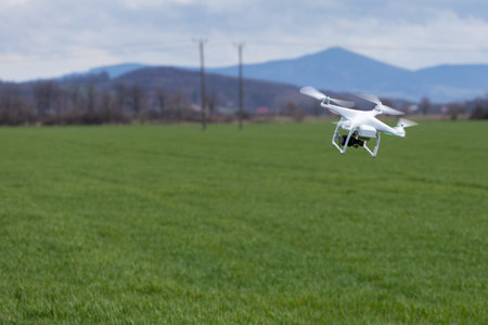 Small drone is flying high above the green field