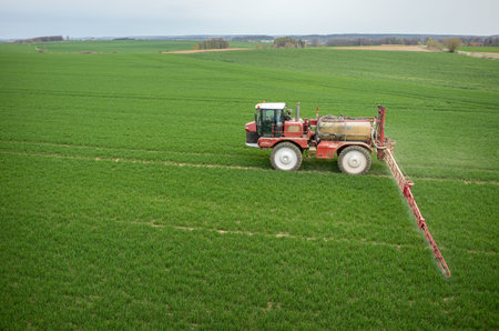 Aerial view of the tractor spraying the chemicals on the large green field