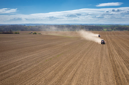 Aerial view of the the tractor harrowing the large brown field in spring season