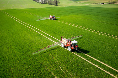 Aerial view of the tractor spraying the chemicals on the large green field