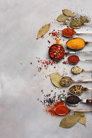 Assorted multicolored condiment in silver spoons on gray backgroundの写真素材