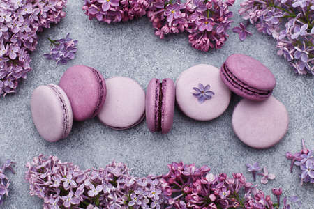 Set of violet and lilac macarons in a row with frame made of lilac flowers on gray concrete background. Top view, flat lay. Food backgroundの写真素材