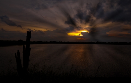 Sunrise and sunbeam on the pond with dark clouds log timber - Silhouettes composition of natureの写真素材