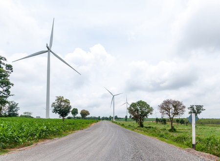 Road way with wind turbines producing power against cloudy sky