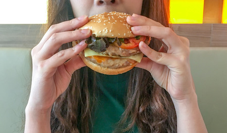 Woman is eating a hamburger with fresh vegetables in the restaurantの写真素材