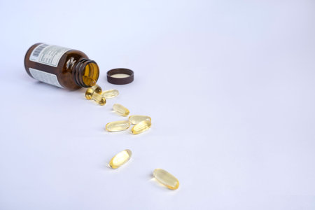 Close up of pills spilling out of brown bottle on white background.